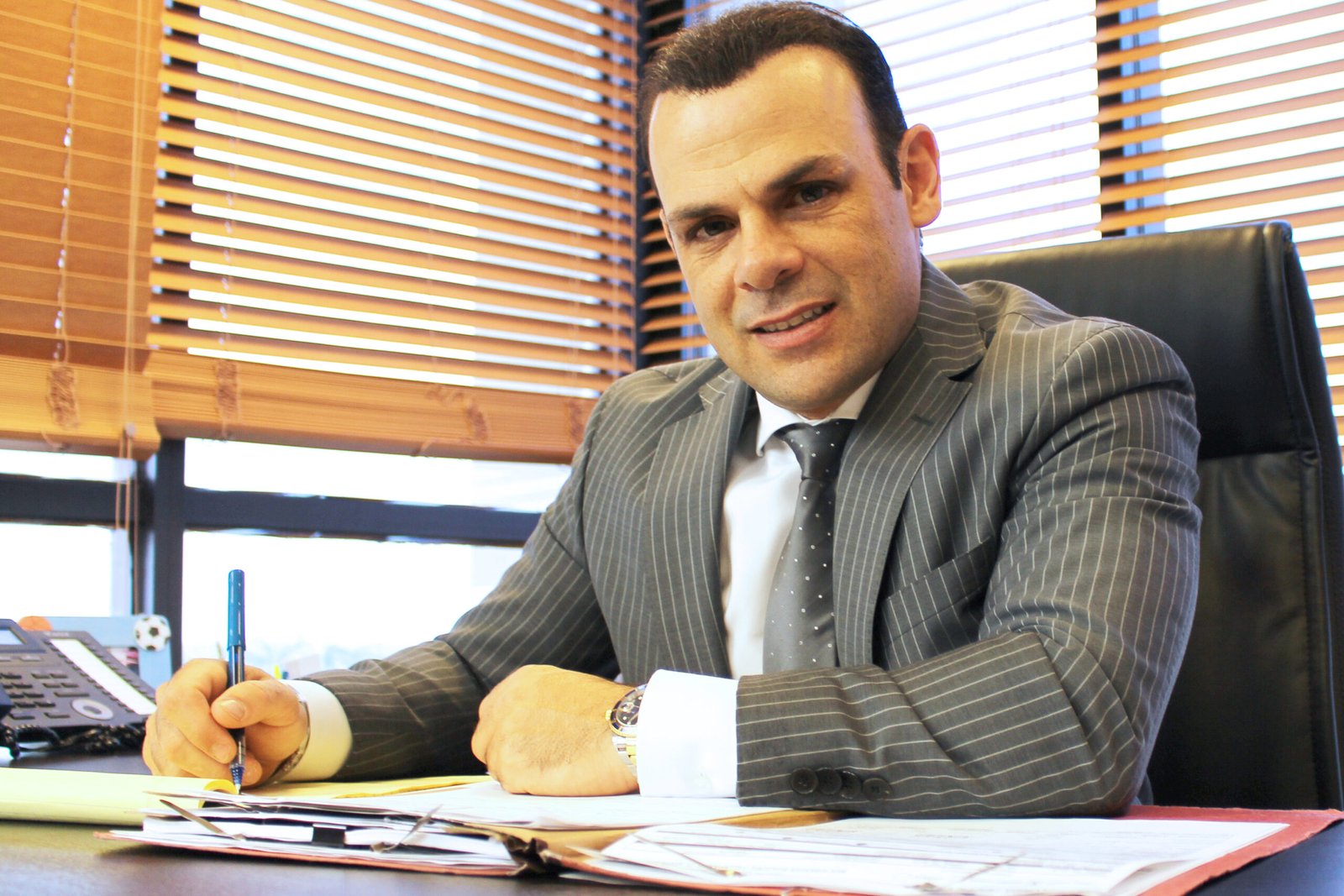 El abogado Big Al mirando a la cámara sonriendo mientras toma notas y trabaja en un caso.